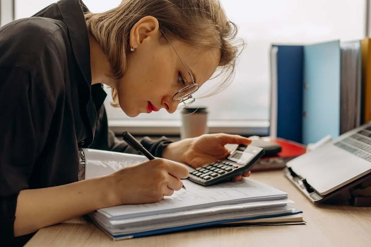 Bookkeeper checking invoice totals on a calculator at her desk