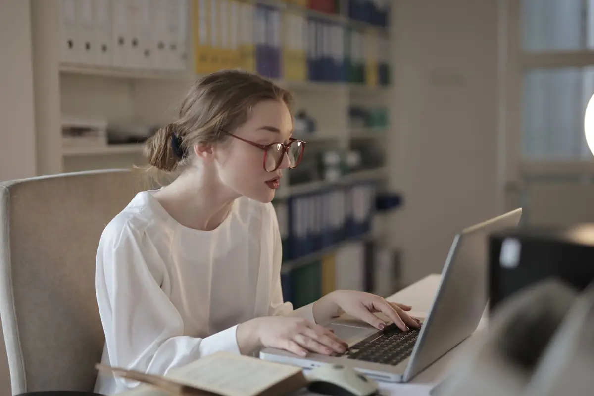 Office worker typing records into a laptop beside rows of files