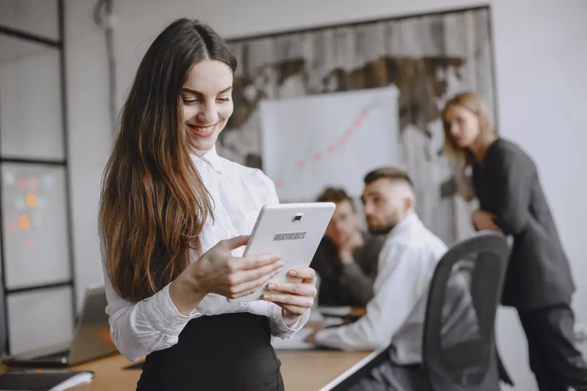 Team member reviewing figures on a tablet while colleagues work behind her