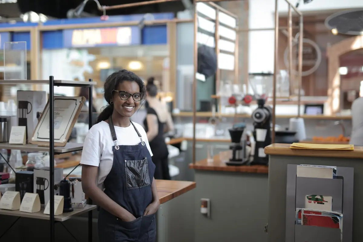 Shop owner in an apron smiling behind the counter of her store