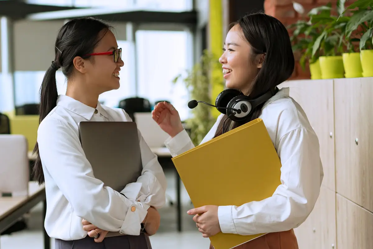 Two colleagues smiling as they hand off paperwork in an office